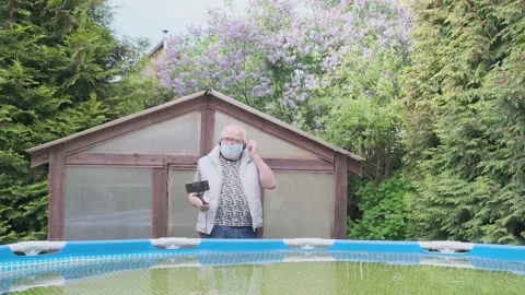 Grey haired man takes off blue mask in country house yard Stock Footage 135442991