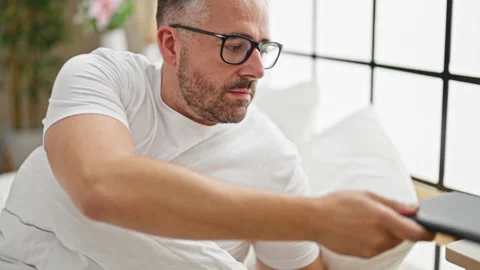 Grey-haired man using touchpad taking glasses off to sleep at bedroom Video stock 246992714
