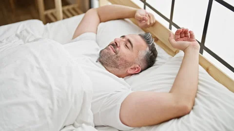 Grey-haired man waking up stretching arms at bedroom Stock Footage 246992699