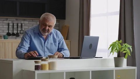 Grey haired man is working at home office, calculating and making report Stock Footage 153517195