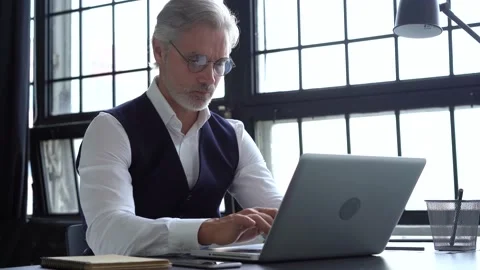 Grey-haired man working on a laptop. Serious mature man in elegant suit typing Stock Footage 140642677