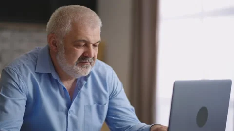 Grey haired man is working with laptop in apartment, typing on keyboard Stock Footage 153511683