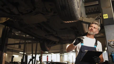 Grey haired mature handsome auto mechanic man in uniform writing to clipboard at Stock Footage 243180292