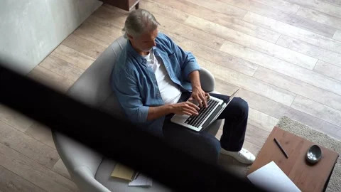 Grey-haired Mature handsome man sitting on sofa and typing on laptop at home Stock-Footage 141184167