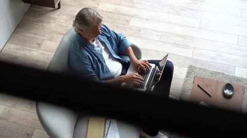 Grey-haired Mature handsome man sitting on sofa and typing on laptop at home Stock Footage 141184180