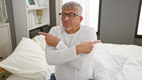 Grey-haired middle age man in pyjamas, pointing fingers in different direct.. Stock Footage 275396835