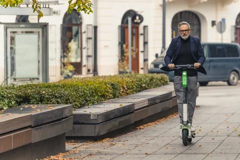 Grey-haired middle aged man in eyeglasses and suit riding rental electric Stock Photos