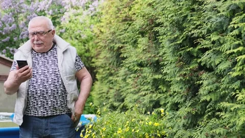Grey haired old man smiles and starts talking on smartphone Stock Footage 136426609