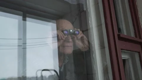 Grey haired old man spy looks through brown outdated window Stock Footage 157878266