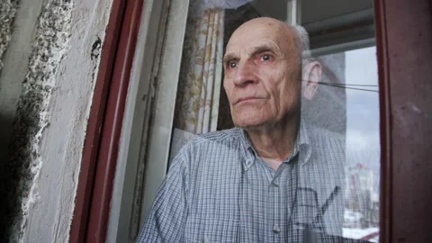 Grey haired senior man stands behind balcony glass and looks with sorrow. Stock Footage 152571332