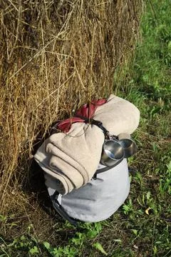Grey hiking backpack with folded blanket and tin mugs leaning against haystack i Stock Photos