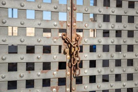 Grey iron gate closed with rusty chain and padlock Stock Photos