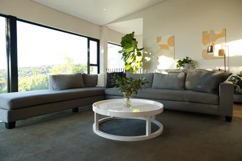 Grey L-shaped sofa is anchoring living room round white coffee table is holding Stock Photos