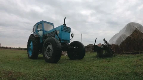 Grey rainy clouds over a vintage blue tractor in the countryside. Unprofitable Stock Footage 143301481