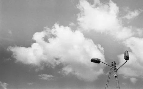 A grey scale low angle shot of lamp posts underneath the beautiful clouds in  Stock Photos