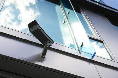 Grey security camera with window reflecting blue sky clouds 库存照片
