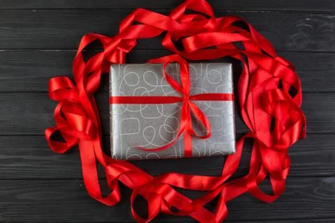 Grey silver gift box with red ribbon bow on black wooden table Stock Photos