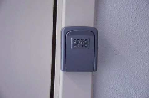 A grey wall mounted key lock box with a combination lock mounted above a tr.. Photos