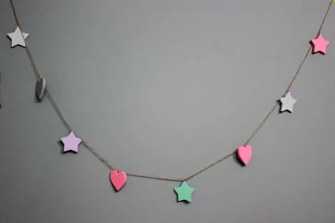 A grey wall with a wooden hand-made garland of stars and hearts in pastel sha Stock Photos