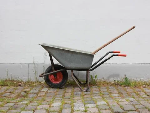 Grey Wheelbarrow on Cobble Surface with Wall Stock Photos