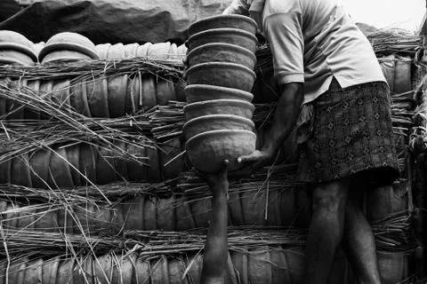 A greyscale of a person holding a stack of clay pots standing near the pots c Foto stock