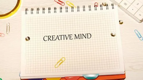 A grid-patterned notebook lies open with the words Creative Mind printed on its Stock Photos