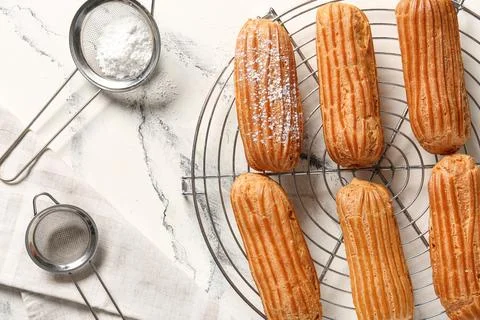 Grid with tasty eclairs, sieves and sugar powder on marble background Stock Photos