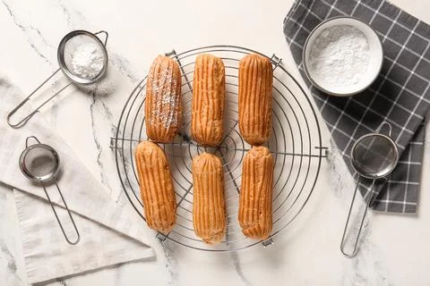Grid with tasty eclairs, sieves and bowl of sugar powder on marble background Stock Photos