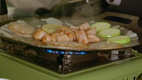 Grill pan lined with parchment paper sizzles on a portable green gas stove. Stock Footage 328617511