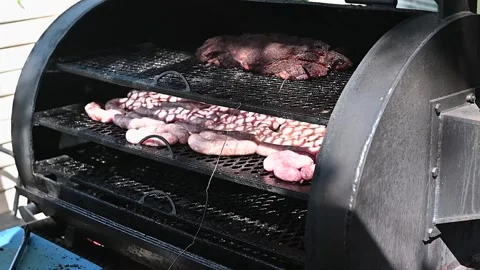 A grill is set up outdoors with multiple racks cooking various cuts of beef and 스톡 동영상 337101263