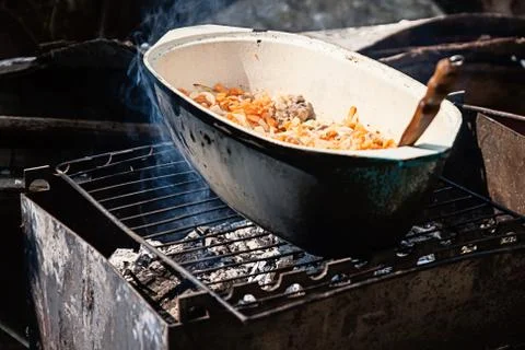 On the grill stands a cauldron in which to prepare meat and vegetables Stock Photos