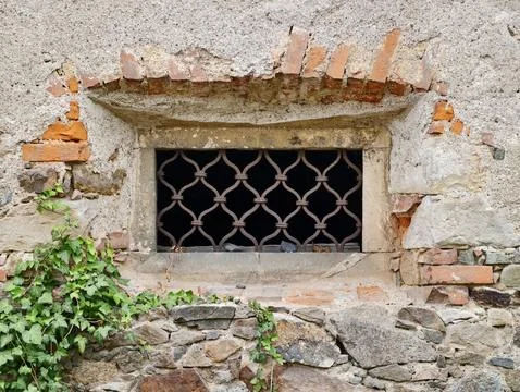 Grilled basement window in weathered stone and plaster wall Stock Photos