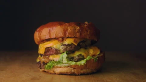 Grilled Beef Burger with Melted Cheese and Fresh Vegetables on a Wooden Table Stock Footage 236576610