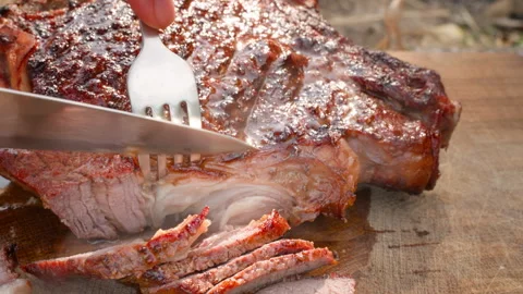 Grilled beef is cut into pieces using a knife on a wooden board. Stock Footage 281233471