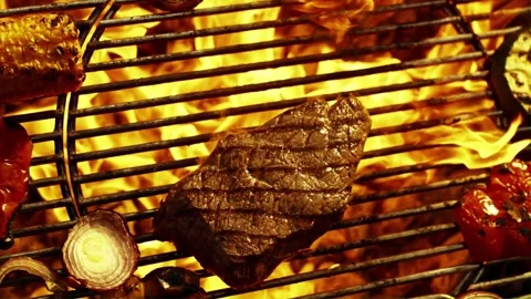 Grilled beef steak on barbecue grate with burning flames and vegetables in .. Stock Footage 345613202