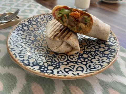 Grilled chicken wrap with vegetables on patterned plate offers delicious lu.. Stock Photos
