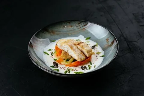 Grilled cod fillet with vegetables and sauce on a black backgrou Stock Photos