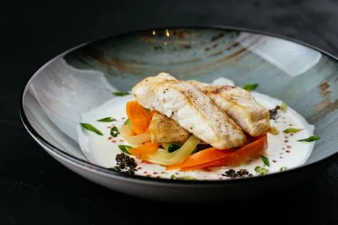Grilled cod fillet with vegetables and sauce on a black backgrou Stock Photos