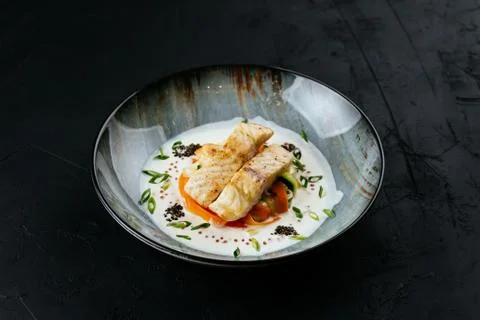 Grilled cod fillet with vegetables and sauce on a black backgrou Stock Photos