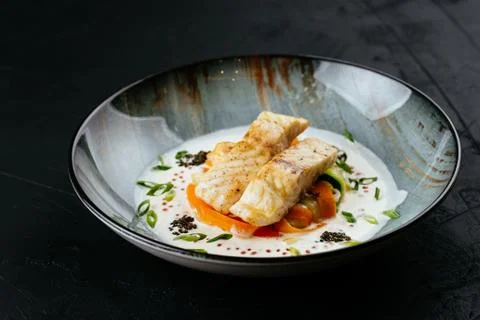 Grilled cod fillet with vegetables and sauce on a black backgrou Stock Photos