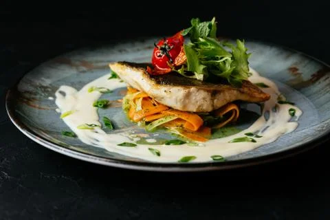 Grilled cod fillet with vegetables and sauce on a black backgrou Stock Photos