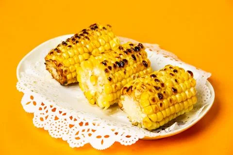 Grilled Corn on the Cob served in plate isolated on orange background side .. Stock Photos