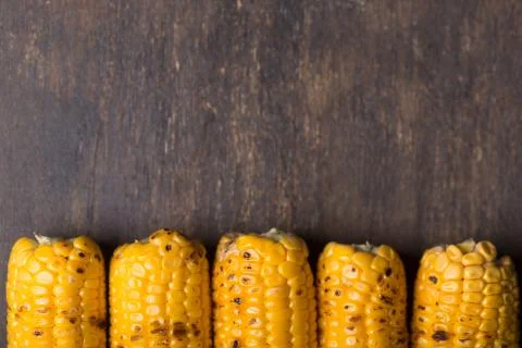 Grilled corn cobs on the brown rustic background. Top view with horizontal co Stock Photos