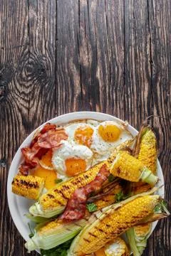 Grilled corn in cobs with fried eggs and bacon Foto stock