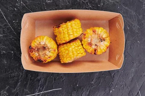 Grilled corn in a craft container on an isolated dark background. Take away Stock Photos