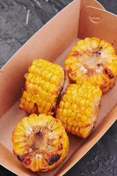 Grilled corn in a craft container on an isolated dark background. Take away Stock Photos