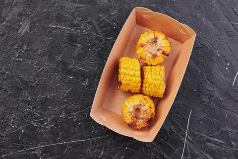 Grilled corn in a craft container on an isolated dark background. Take away Stock Photos