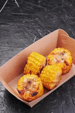 Grilled corn in a craft container on an isolated dark background. Take away Stock Photos