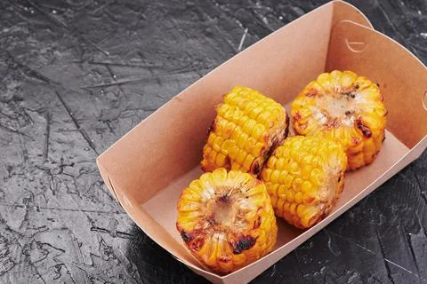 Grilled corn in a craft container on an isolated dark background. Take away Stock Photos