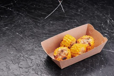 Grilled corn in a craft container on an isolated dark background. Take away Stock-Fotos